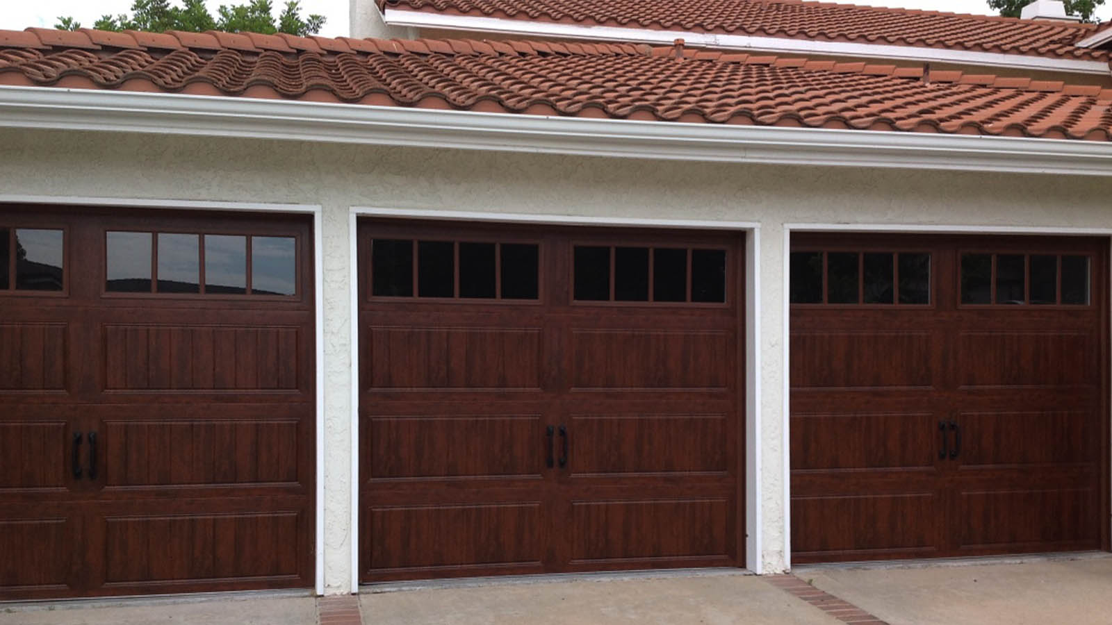 Spanish-style home with rich mahogany garage doors, classic window panels, and terra cotta tile roofing.