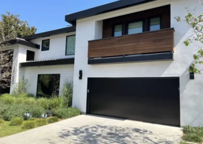A sleek, two-story modern house with a large, solid black garage door and wood accents on the second floor.