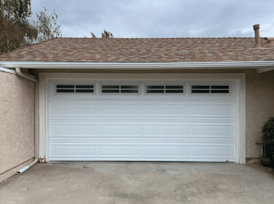 Classic white sectional garage door with raised panel design and five rectangular windows across the top, installed on a suburban home in Studio City area under cloudy skies
