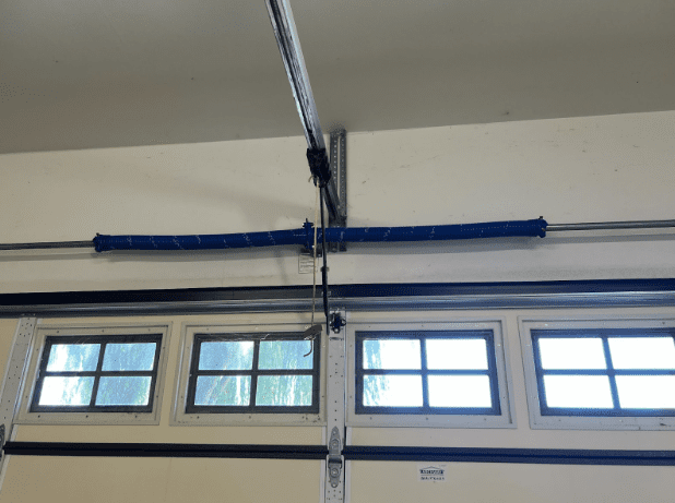 Interior view of residential garage doors and garage door openers showing a newly repaired dual blue torsion spring system and overhead rail.